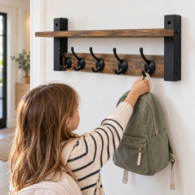 Fillette accrochant un sac à dos vert à l’étagère porte-manteau murale Cassandra en bois brun, avec cinq crochets noirs.